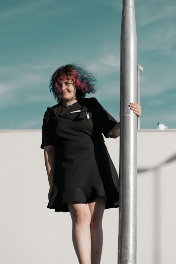 Woman in Black Dress Holding on Pole