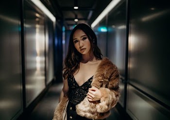 woman in black floral sleeveless top and brown fur coat standing between gray walls