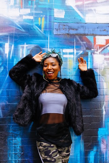 Woman in Black Fur Jacket Leaning on Wall and Smiling