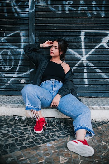 Woman in Black Jacket and Blue Jeans Sitting Near Roller Shutter