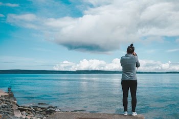woman in black jeans standing and holding camera capturing view of large body of water during daytime