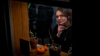 Woman in Black Long-sleeved Shirt Standing Beside Brown Wooden Window With Three Plants in Pots