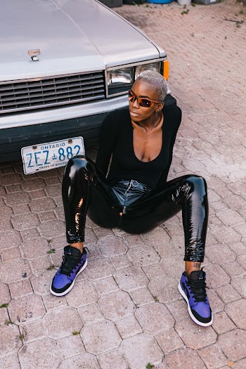 Woman in black scoop-neck long-sleeved shirt sitting down in front of parked car
