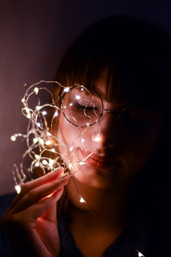 Woman in Black Shirt Leaning on Wall Holding Light Strings