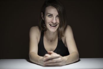 Woman in Black Sleeveless Top Leaning on White Table Smiling