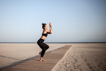 Woman in Black Sports Bra and Leggings Doing Yoga in Brown Wooden Mat in Beach