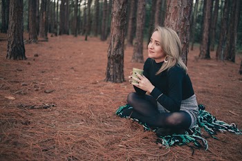 Woman in Black Sweater Sitting on Brown Ground While Holding Cup