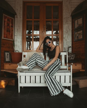 Woman in Black Tank Top and Black-and-white Stripe Pants Sitting on White Wooden Bench While Holding Head