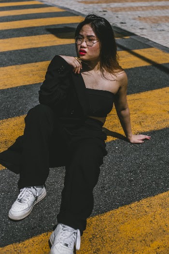 Woman in Black Top and Black Pants Sitting on Pedestrian Lane