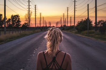 woman in black top walking on grey asphalt road during sunset