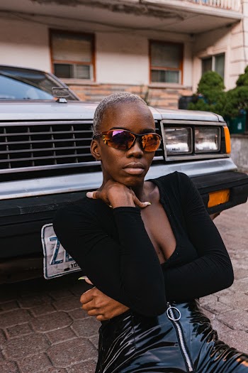 Woman in black v-neck top sitting down in front of parked car