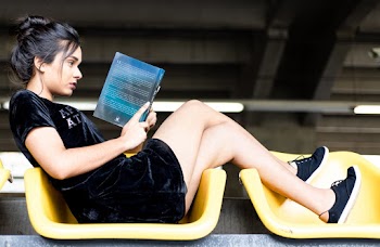 Woman in Black Velvet Dress and Black Sneakers Reading Book