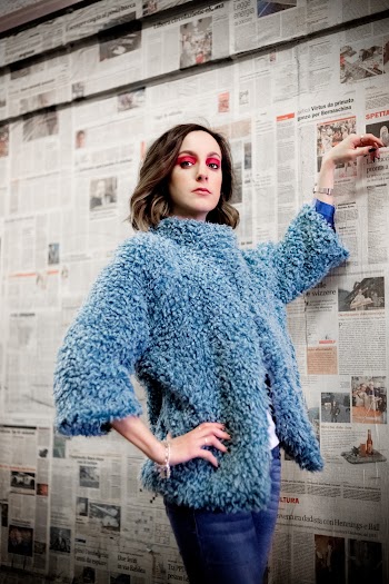 Woman in Blue and White Coat and Blue Denim Jeans Holding Wall Covered in Newspaper Pages