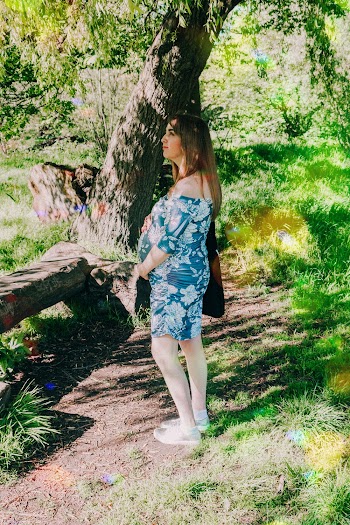 Woman in Blue and White Floral Maternity Dress Standing Under Tree