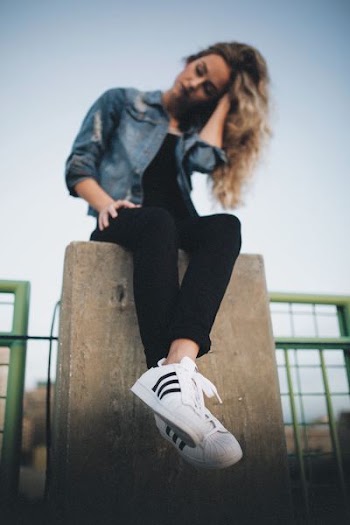 woman in blue denim button-up jacket and black pants sitting on gray concrete post during daytime