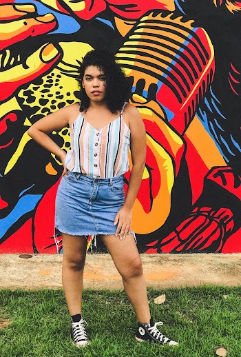 Woman in Blue Denim Miniskirt Holds Waist and Stands in Front of Graffiti Wall