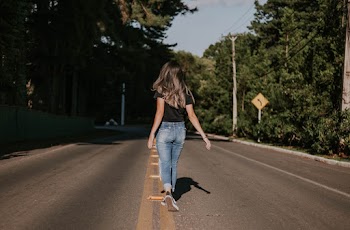 Woman in Blue Denim Pants Walking on Road Near Trees