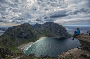 Woman in Blue Jacket and Black Pants Sitting on Ledge Overlooking Bay