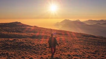 woman in blue jacket walking on desert during sunset