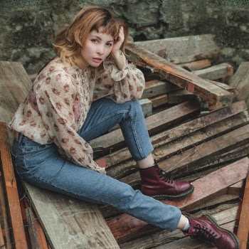 Woman In Blue Jeans Sitting On Pile Of Wood