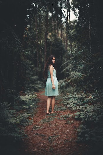 Woman in Blue Sleeveless Dress Walking Between Green Trees Inside Forest