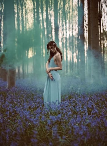 woman in blue spaghetti strap dress standing in the middle of forest