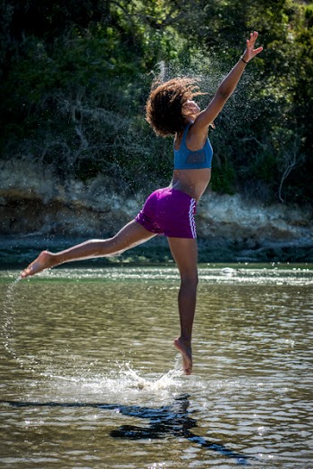 Woman in Blue Sports Bra and Purple Shorts Leaping Above Body of Water
