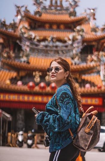 Woman in Blue Sweater and Sun Glasses Standing in front of Temple