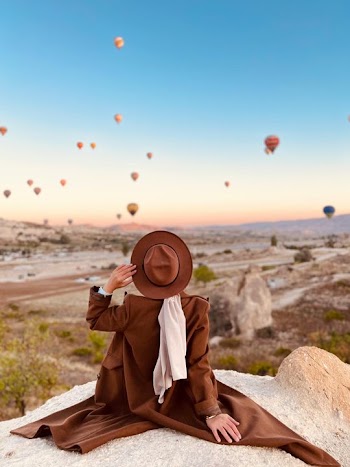Woman in Brown Coat Watching Hot Air Balloons at Sunrise in Cappadocia