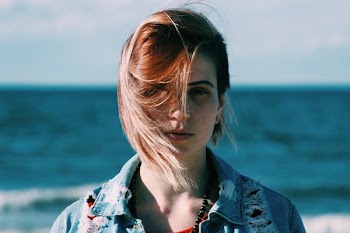 woman in brown denim jacket standing near on beach during daytime shallow focus photography