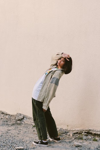 Woman in Brown Jacket and Black Pants Standing Near Concrete Wall