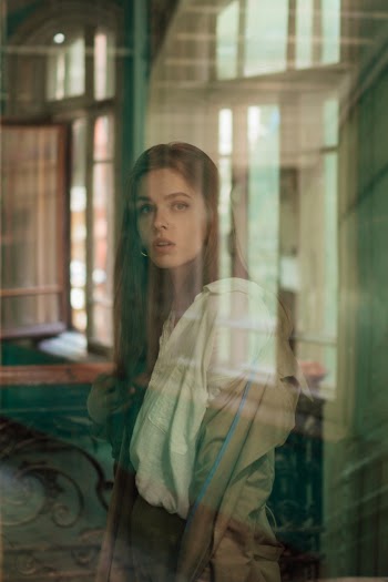 Woman in Brown Jacket and White Collared Button-up Shirt Facing A Glass Window