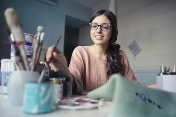 Woman in Brown Long-sleeved Shirt Wearing Eyeglasses Holding Paint Brush