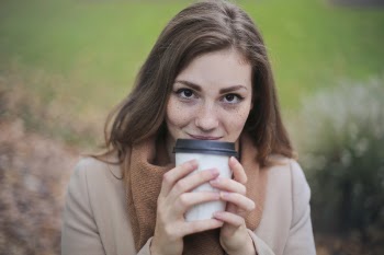 Woman in Brown Top and Scarf Holding a White and Black Travel Cup Outside