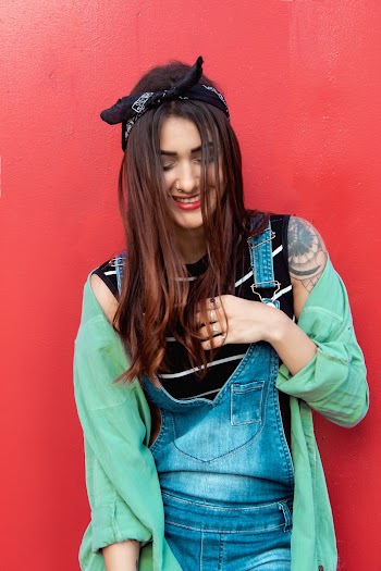 Woman in denim Dungaree Jumpsuits and Teal Jacket in Front of Red Wall