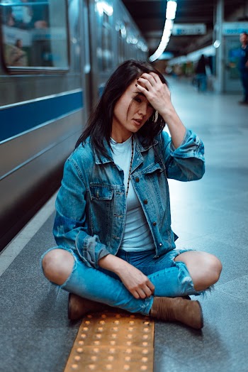 Woman in Denim Jeans and Jacket Sitting Beside a Bullet Train