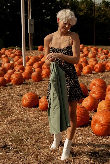 Woman in Floral Dress Standing Near Orange Pumpkins