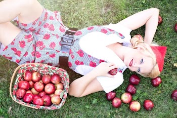 Woman in Gray and White Rose Print Onesies Laying on Grass Beside Red Apple Fruits