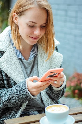 Woman in Gray Coat Sitting While Using Smartphone