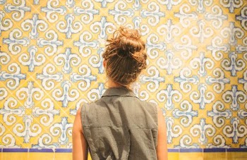 woman in gray collared sleeveless top facing white and yellow floral wall