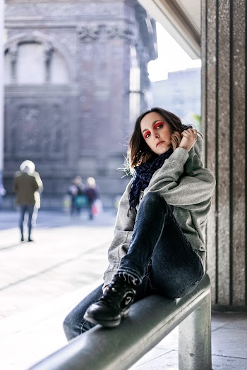 Woman in Gray Jacket and Blue Denim Jeans Sitting on Gray Metal Bracket
