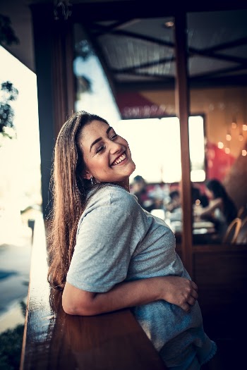 Woman in Gray Shirt Leaning on Chair While Smiling