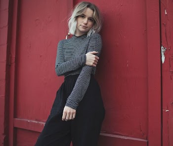 woman in gray top leaning her back on red wall