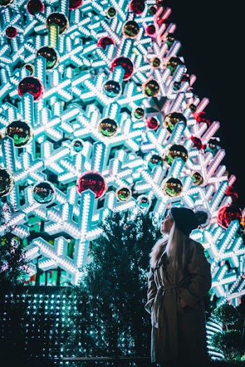 woman in gray trench coat standing near Christmas tree outdoors