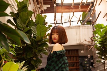Woman In Green And Black Gingham Shirt Standing In Front Of Green Plant