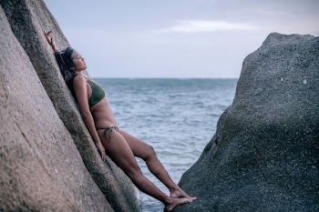 woman in green bikini leaning on gray stone formation