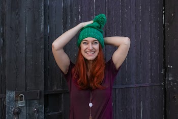 Woman in Green Bobble Cap and Purple T-shirt Posing Near Black Wooden Fence