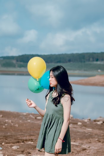 Woman in Green Sleeveless Dress Holding Yellow, Green, and Blue Balloons