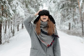 Woman in Grey Coat Holds Cap and Stands in the Middle of Snow Covered Ground