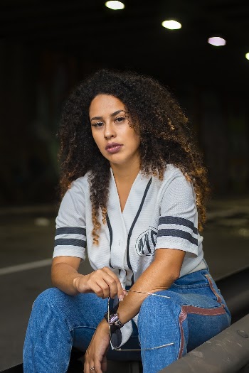 Woman in Grey Shirt and Blue Jeans Sits on Side of Road